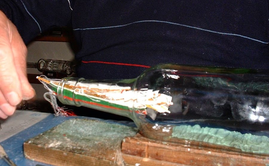 Das zusammengeklappte Segelschiff wird in die Buddel geschoben.